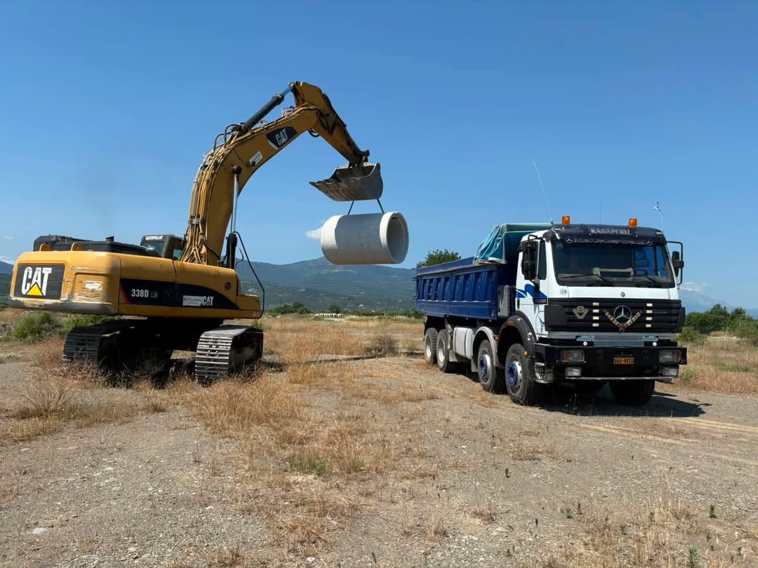 Εκσκαφέας CAT ανυψώνει σωλήνα δίπλα σε φορτηγό Kathargios