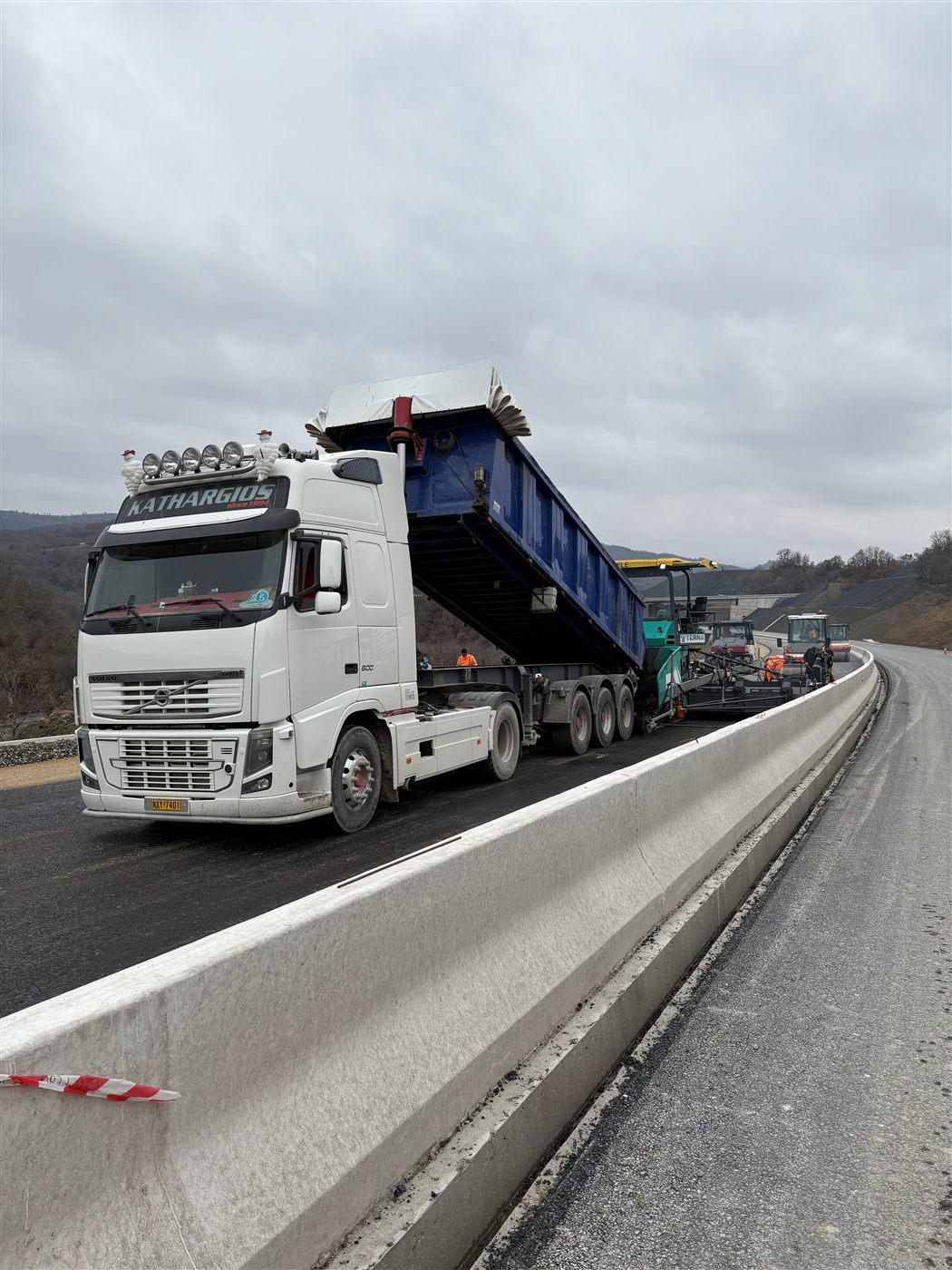 Φορτηγό Kathargios Group σε έργο οδοποιίας — εκφόρτωση υλικού σε ασφαλτοστρωτήρα